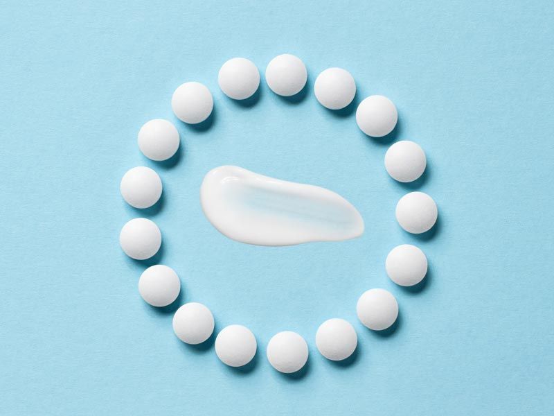 A cream swatch and round white pills on a light blue surface