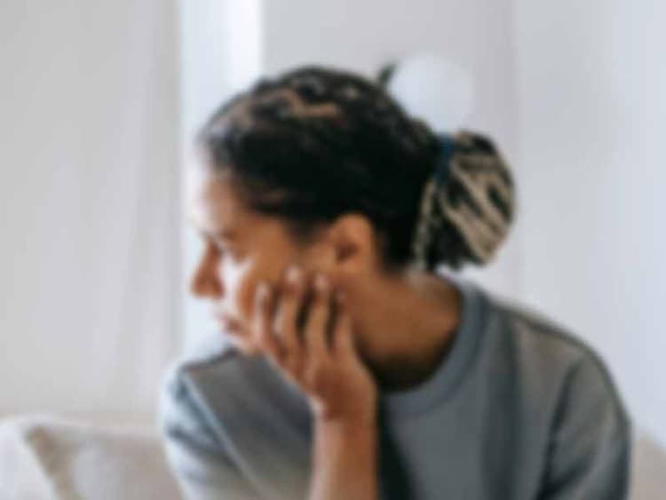 A woman looking concerned while wearing a gray sweater and sitting on a white sofa