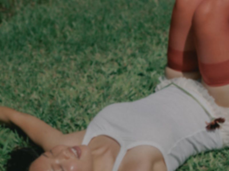 Woman lying relaxed in grass with eyes closed, smiling peacefully, representing relief and comfort while managing a UTI.