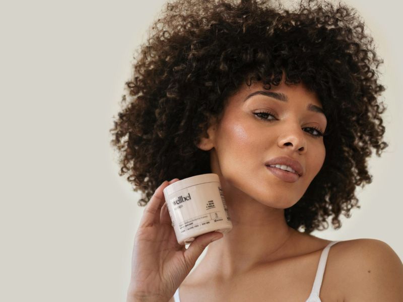 A woman holding a bottle of Wellbel hair supplements