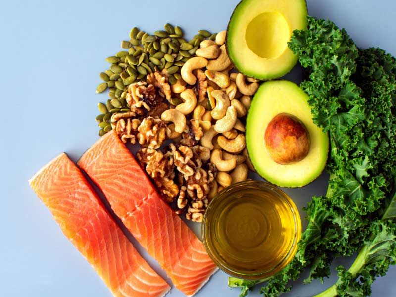 Fish, leafy greens, avocado and nuts on a light blue surface