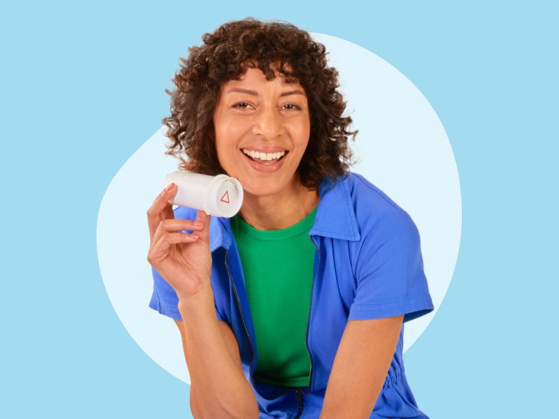 A woman wearing a green shirt and dark blue top is holding a bottle of spironolactone on a light blue background