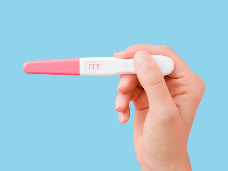 A woman's hand holding a pregnancy test in front of a light blue background