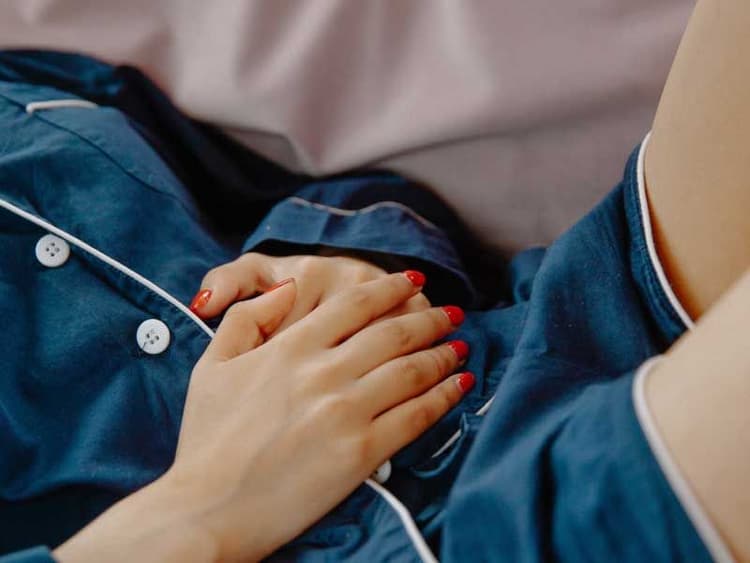 A woman with red nails wearing dark blue pajamas has her hands over her abdomen