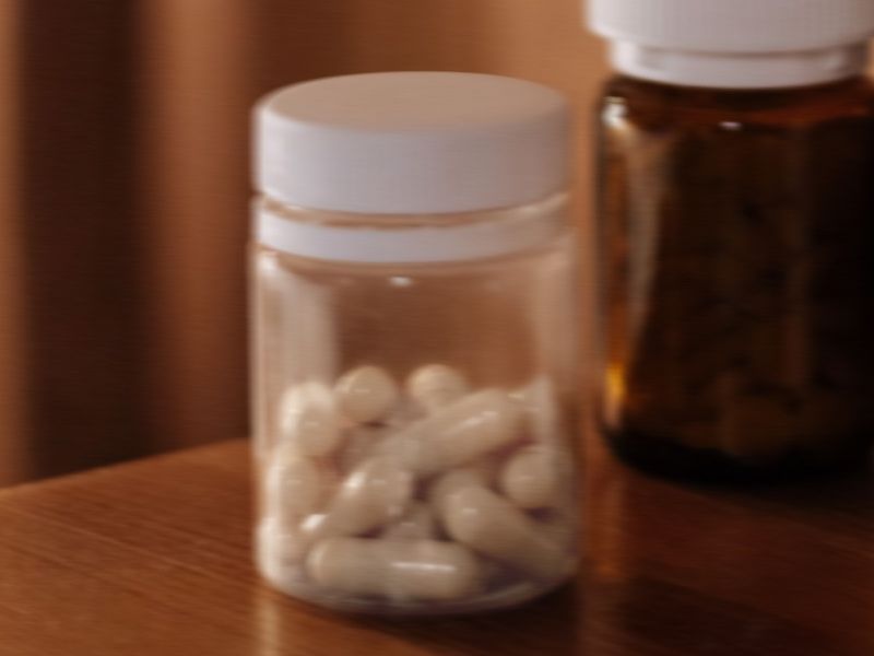 image of a clear, blurry bottle with white capsules on a brown wooden desk