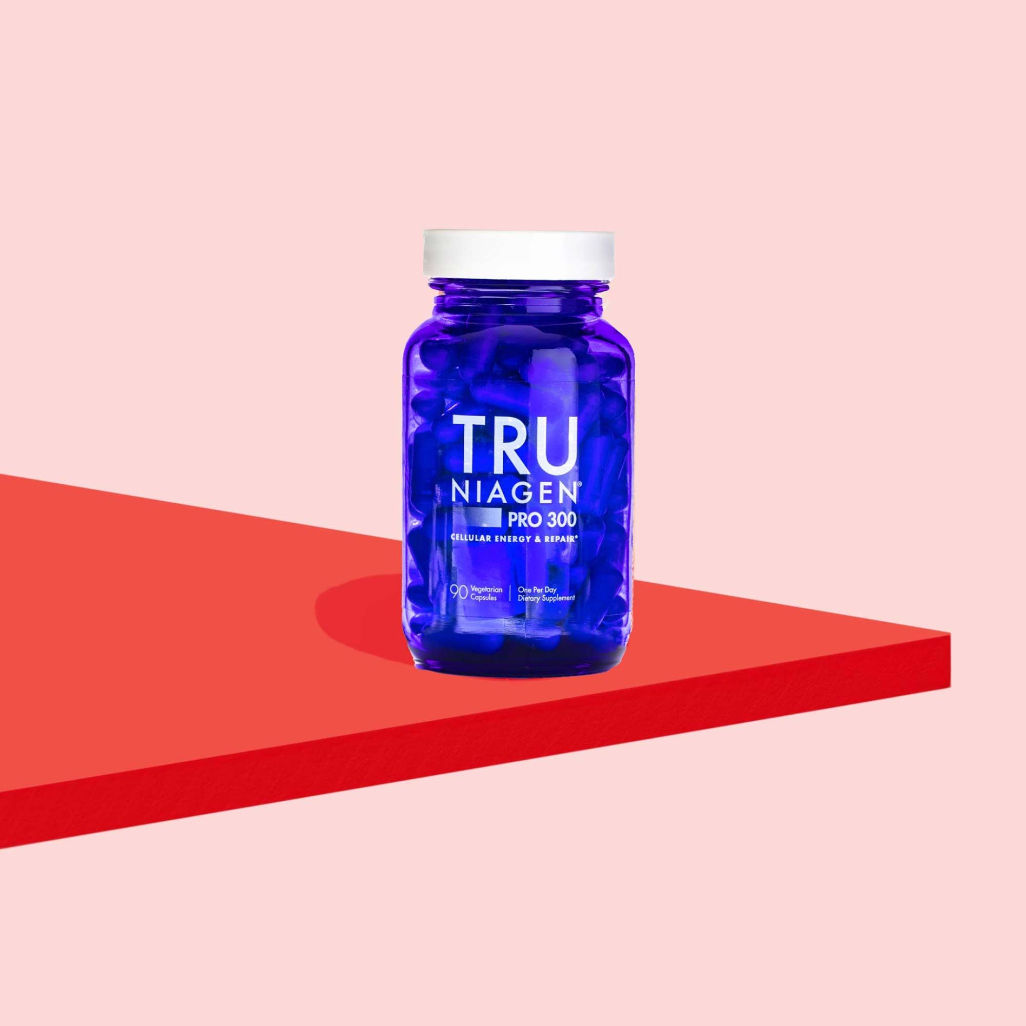 A blue Tru Niagen pill bottle on a red surface with a pink background