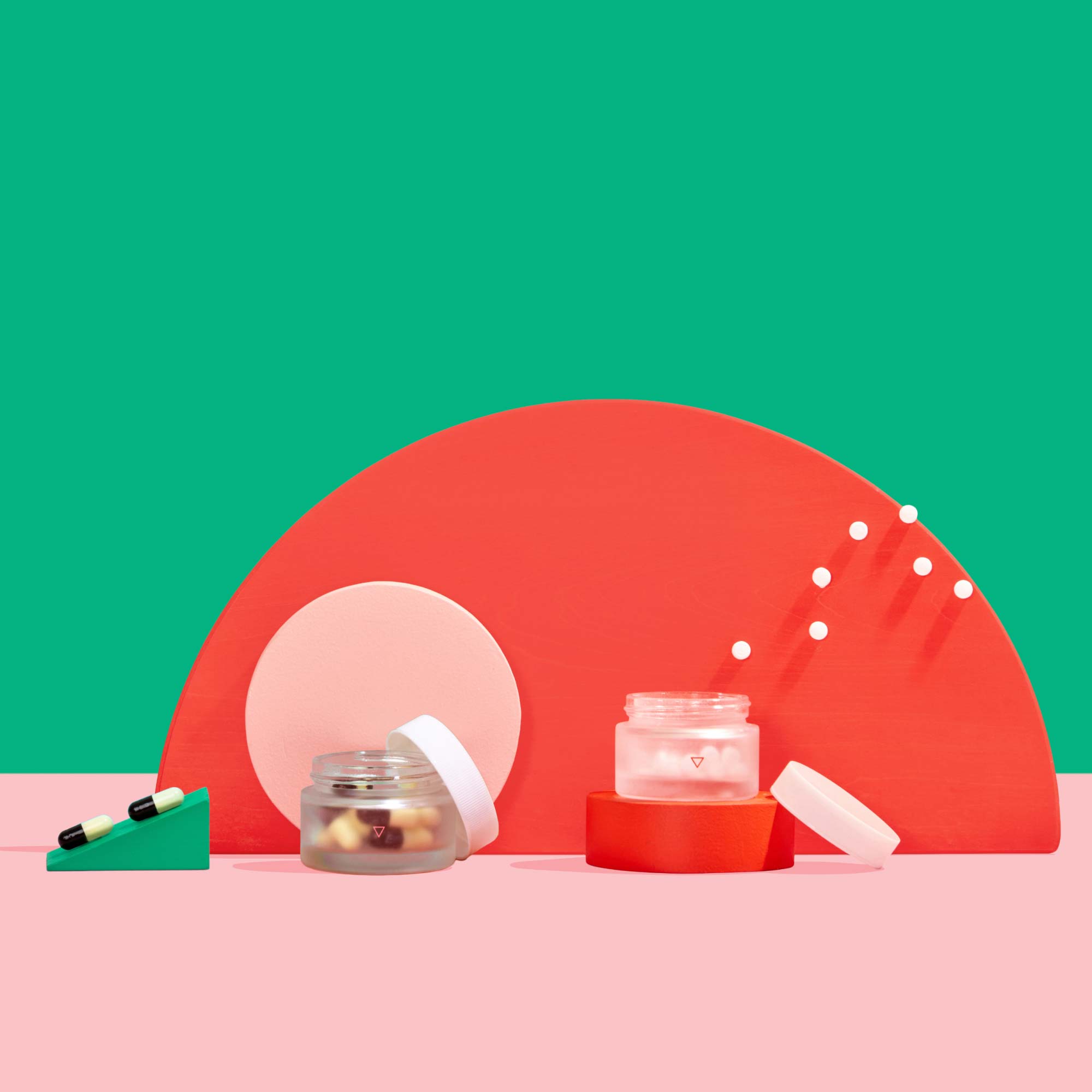 Wisp small glass pill jars with pills floating out balanced on colorful abstract shapes on a pink surface with a green background
