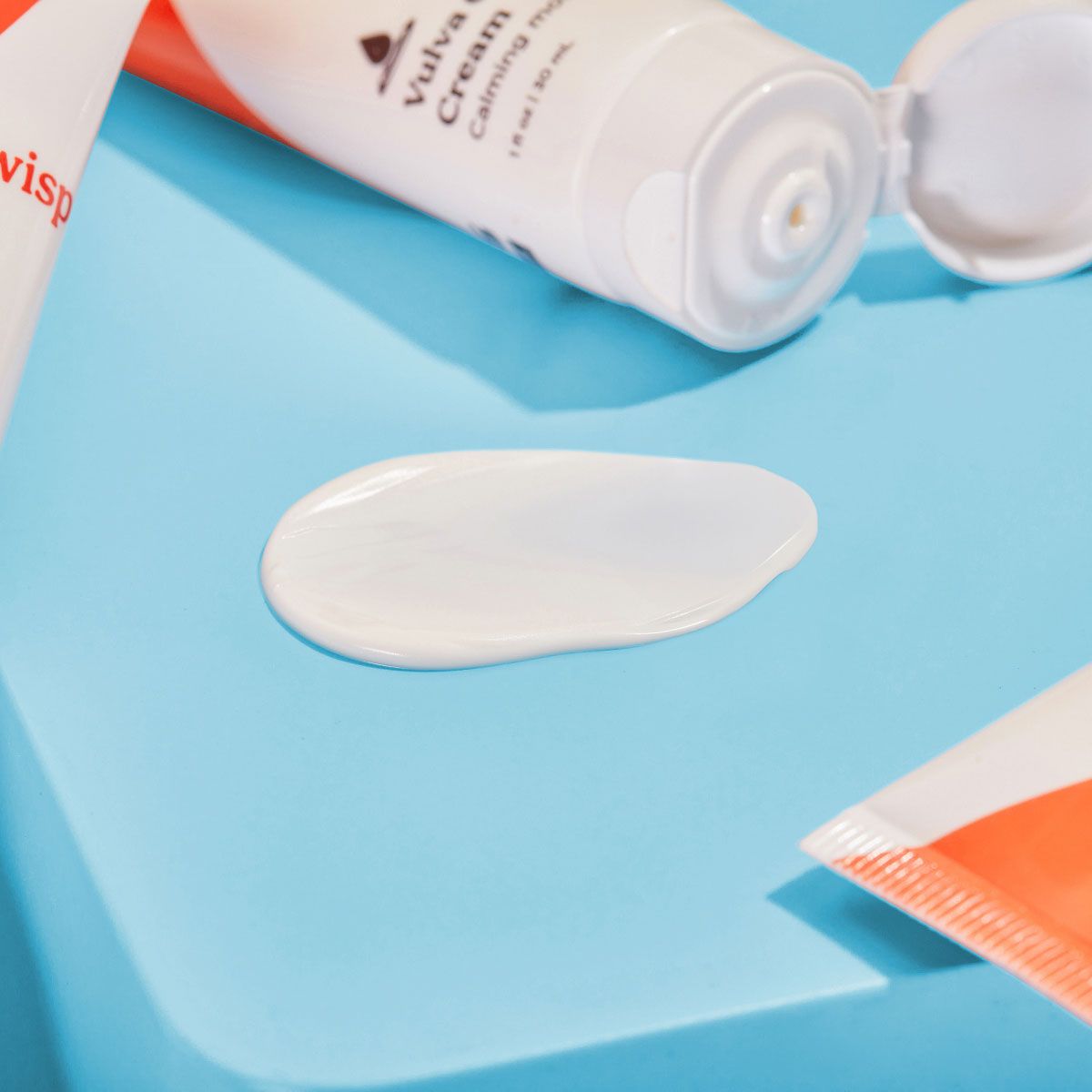A swatch of Wisp Vulva Coco Cream on a light blue surface with multiple open bottles stacked around it