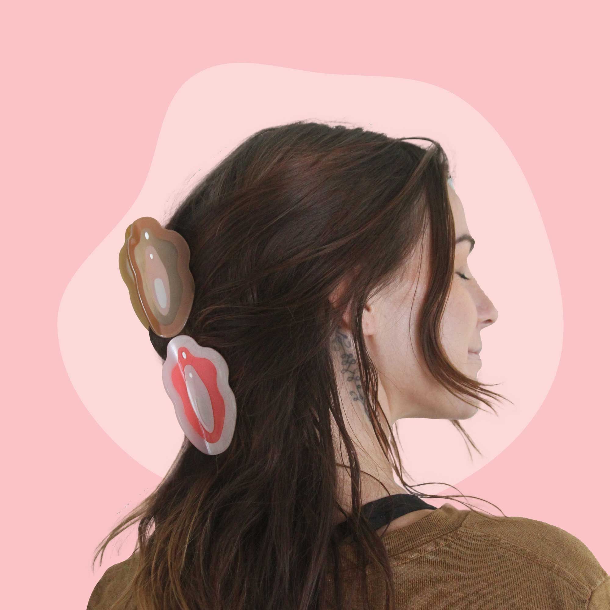 A woman with brown hair is wearing brown and pink vulva clips in her hair
