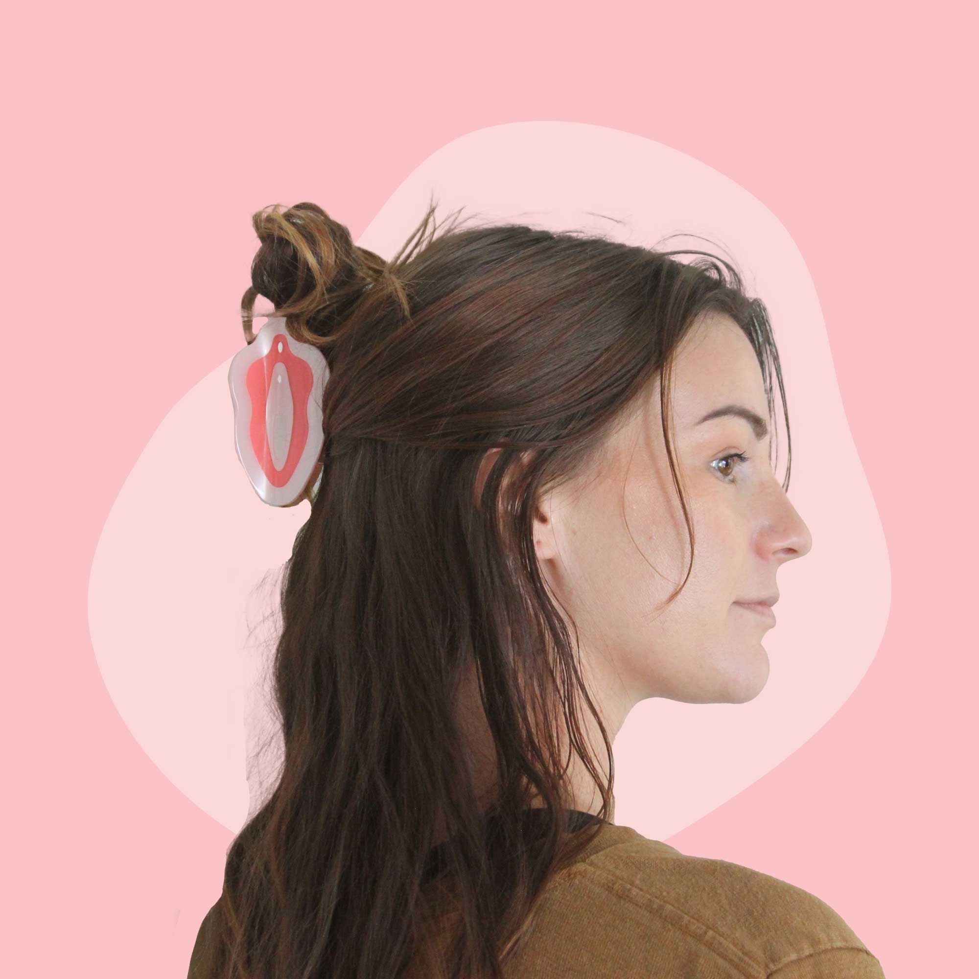 A woman with brown hair is wearing a pink and red vulva clip in her hair