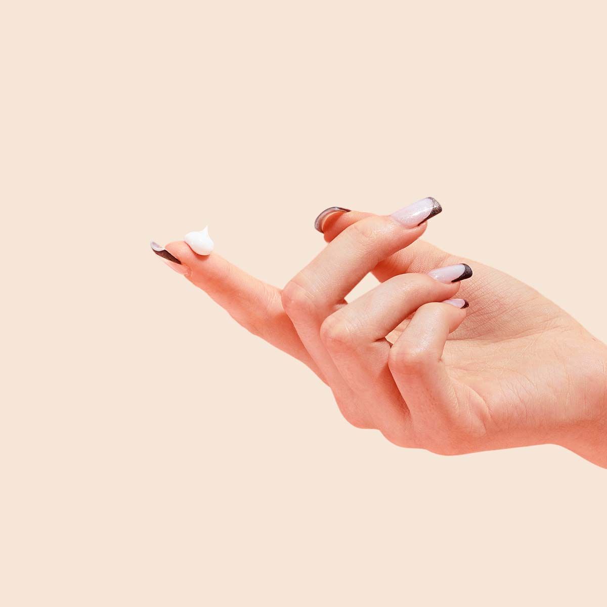 A woman's hand with Vulva Coco Cream on her fingertip with a cream background