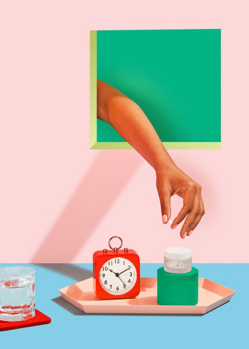 Hand reaching for Norethindrone Acetate with an alarm clock, glass of water and colorful abstract shapes on a red, pink, and light blue background