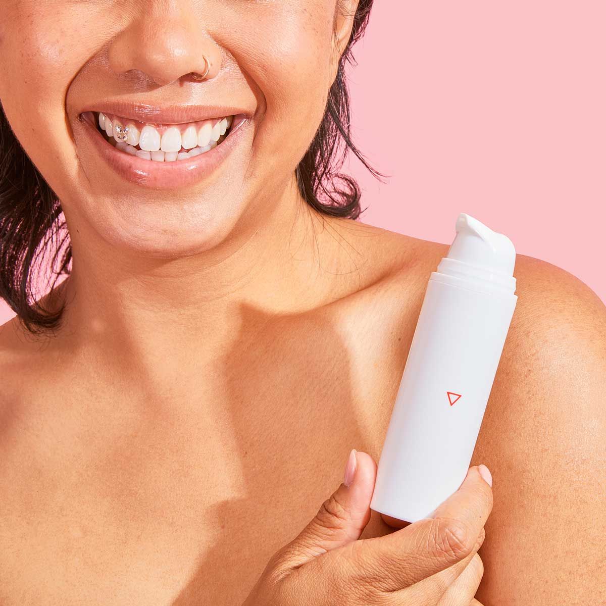 A woman is smiling and whole Wisp's Whole Body Deodorant in front of a pink background