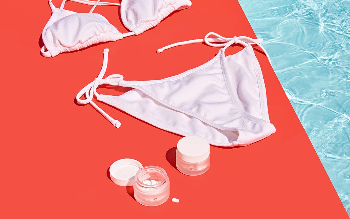 Wisp jars sitting next to a white bikini and sunglasses on a red surface by a pool