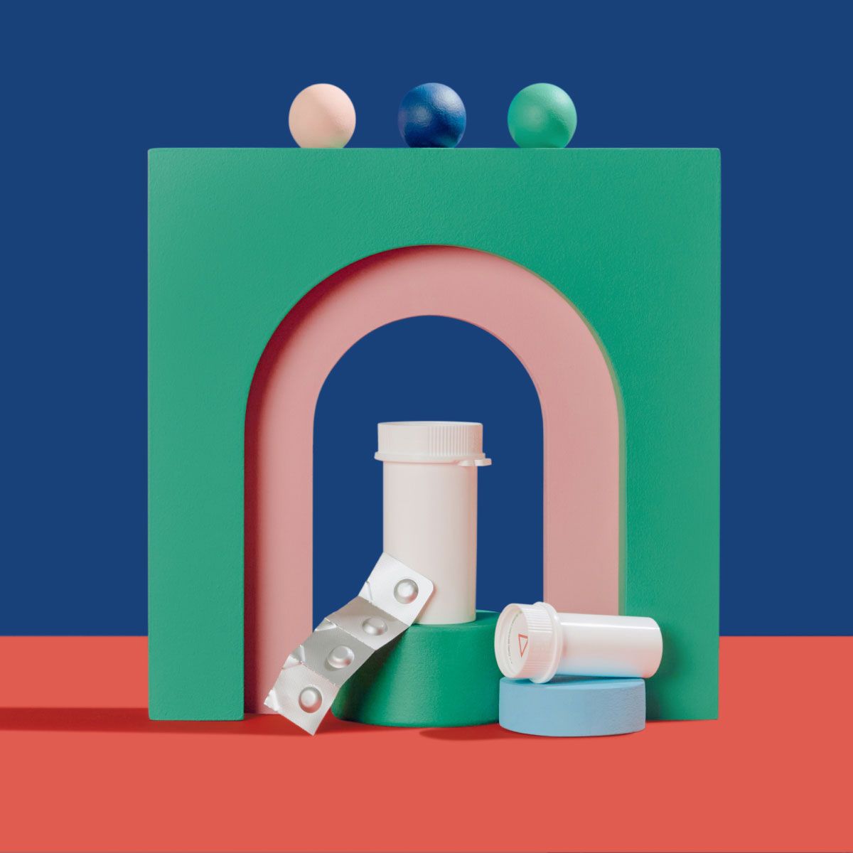 A Zofran pill packet and two pill vials balanced on colorful abstract shapes on a red surface with a blue background