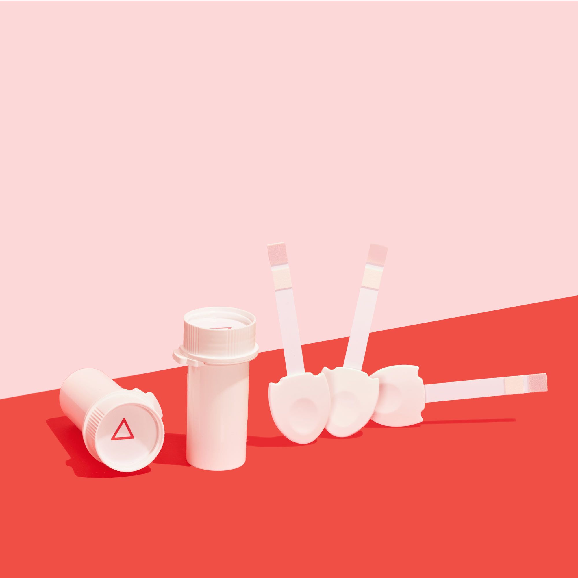 Two Wisp plastic pill vials next two 3 UTI testing strips on a red surface with a pink background