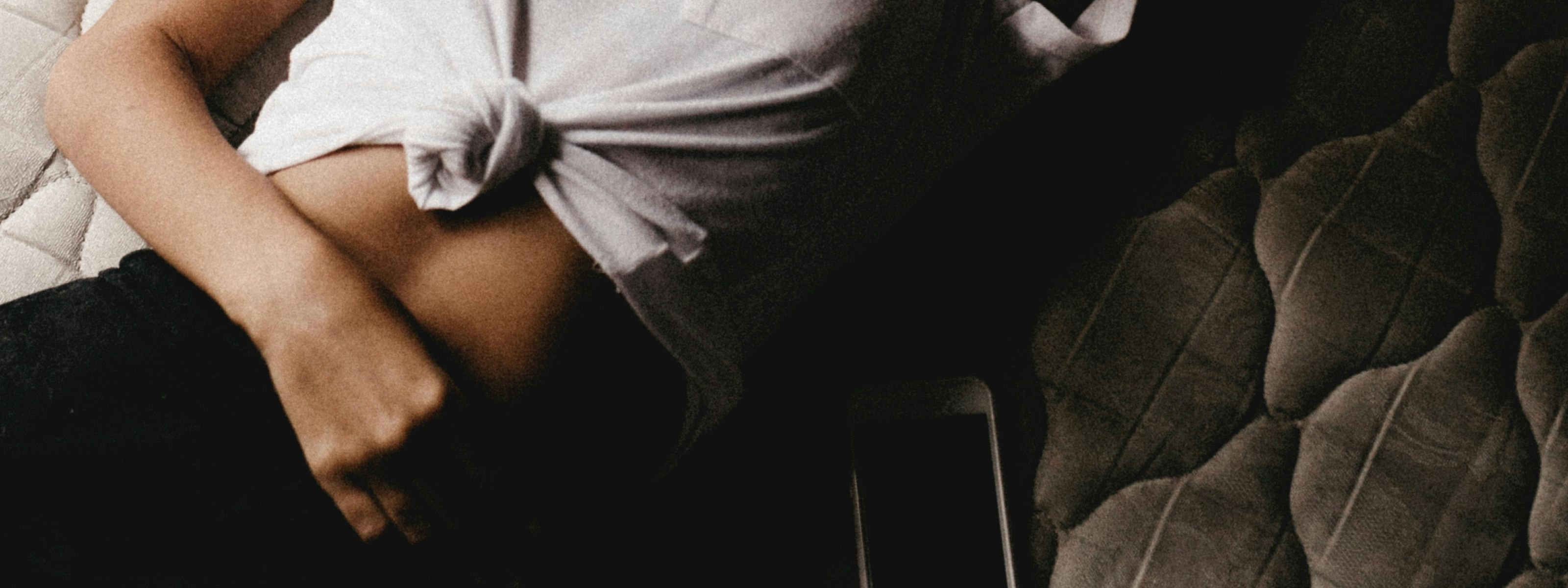 Person lying with shirt tied up, hand on waist, phone nearby.