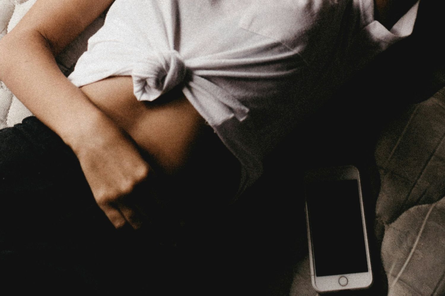 Person lying with shirt tied up, hand on waist, phone nearby.