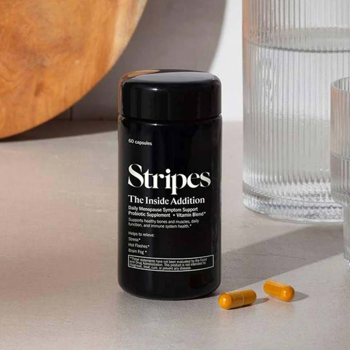 The Inside Addition by Stripes Beauty on a countertop with 2 pills and a glass of water