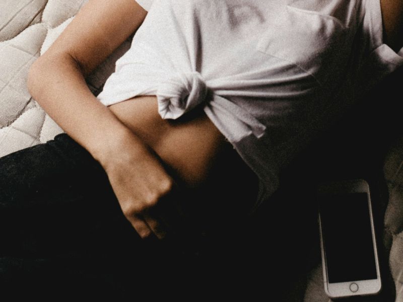 Person lying with shirt tied up, hand on waist, phone nearby.
