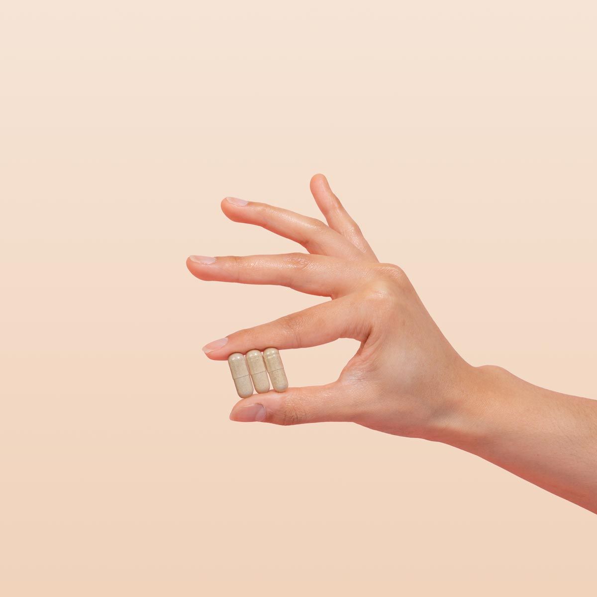 Female hand holding AV Defender capsules on a cream background