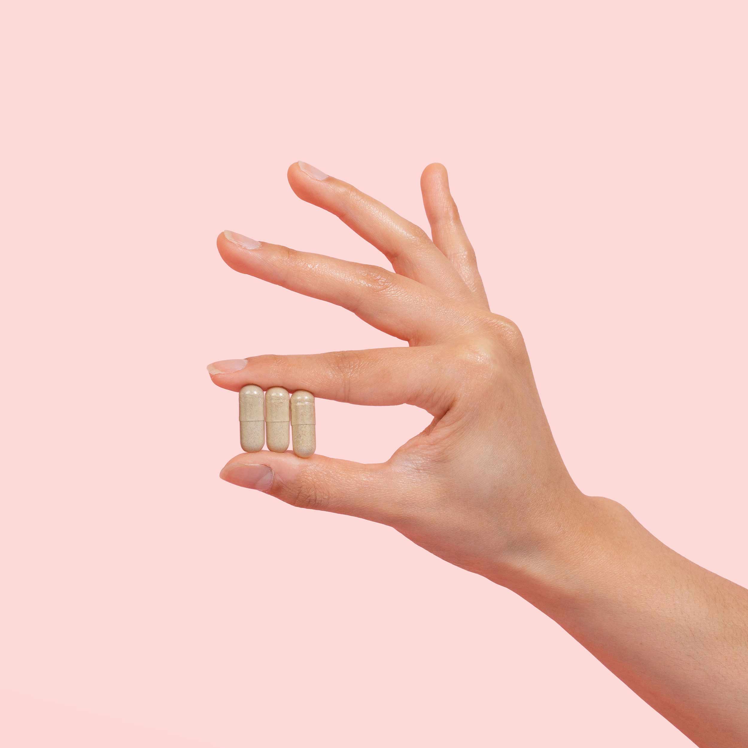 Female hand holding AV Defender capsules on a pink background