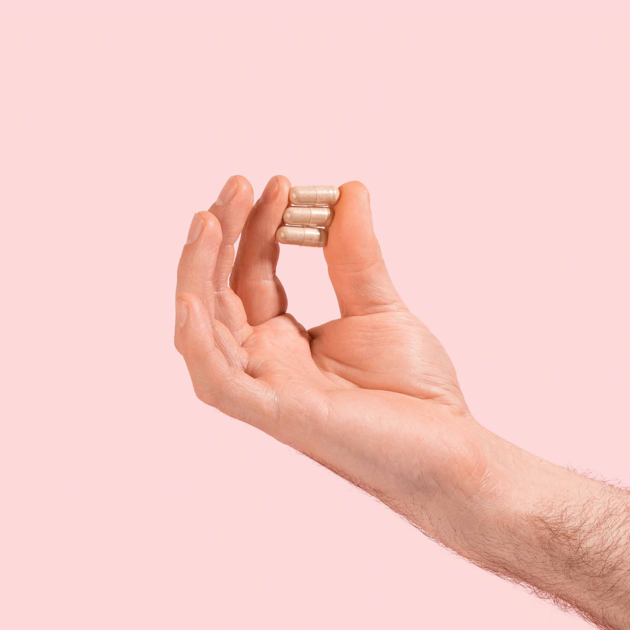 Male hand holding AV Defender capsules on a pink background