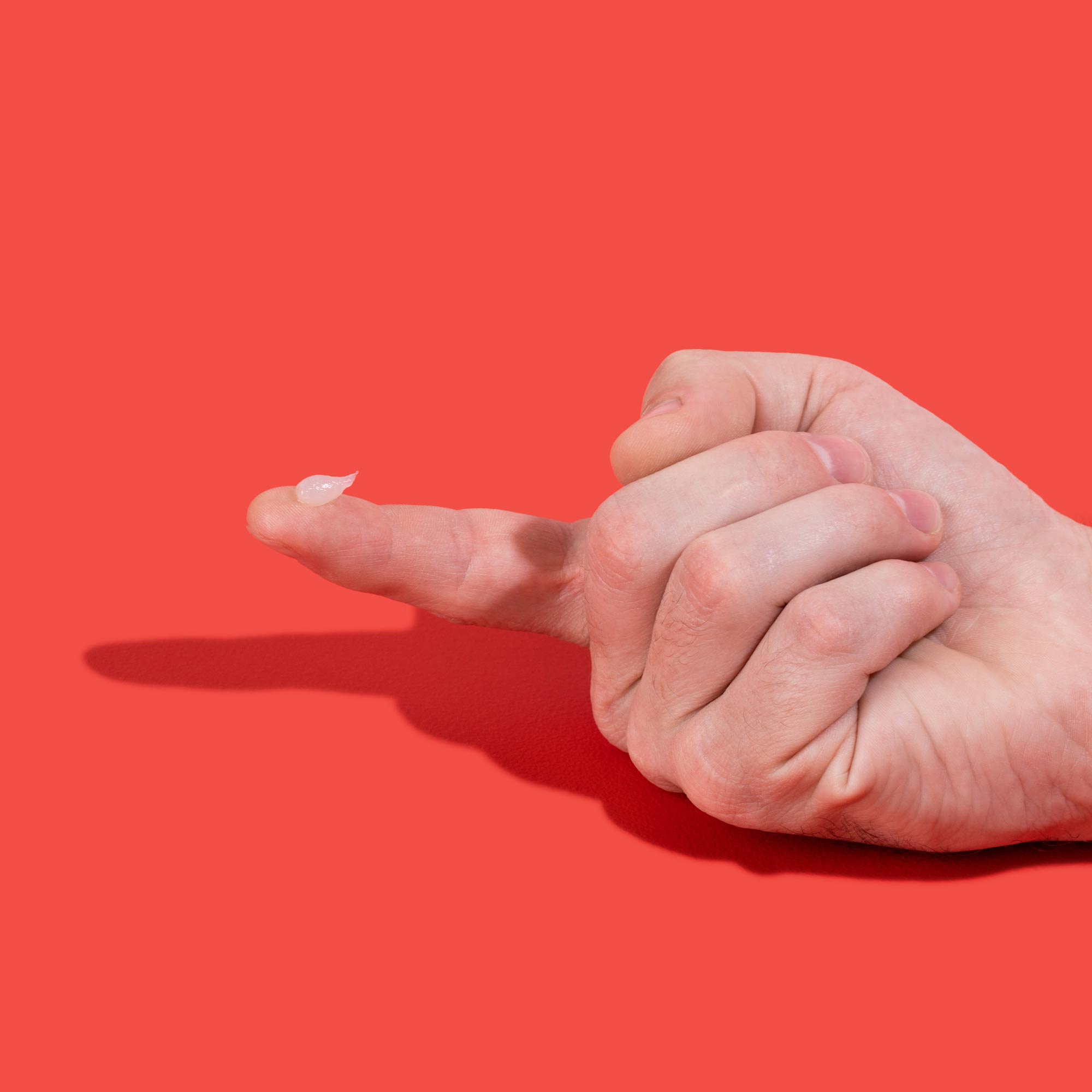 Hand with Acyclovir cream on index finger to treat oral and genital herpes on a red background