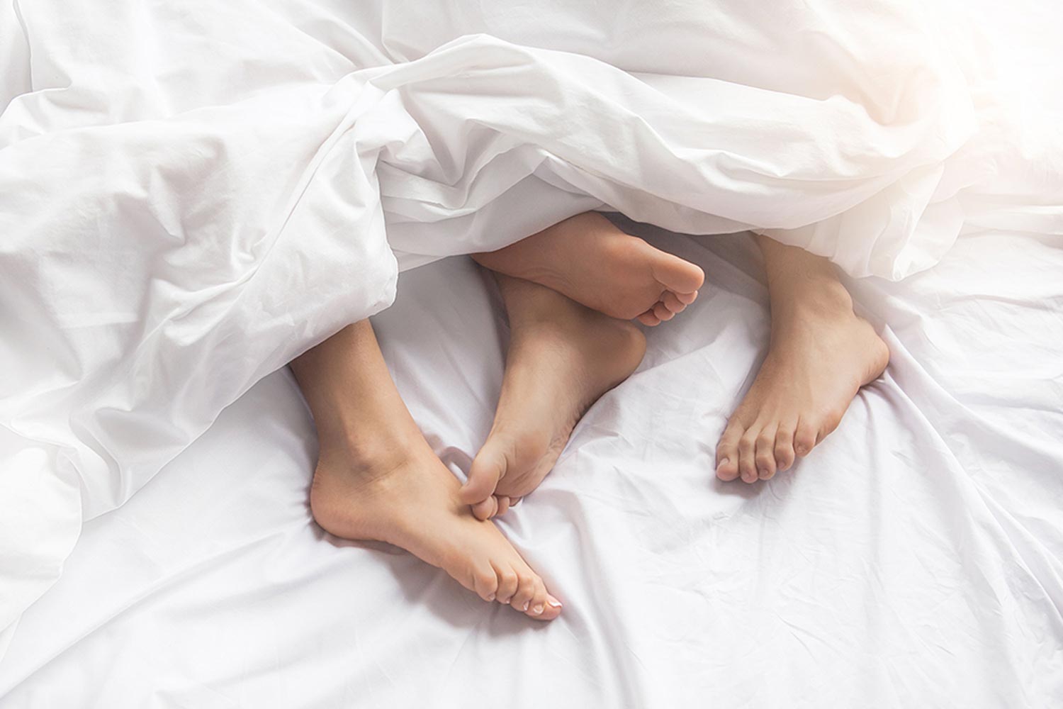A couple's feet in bed hanging out of the sheets