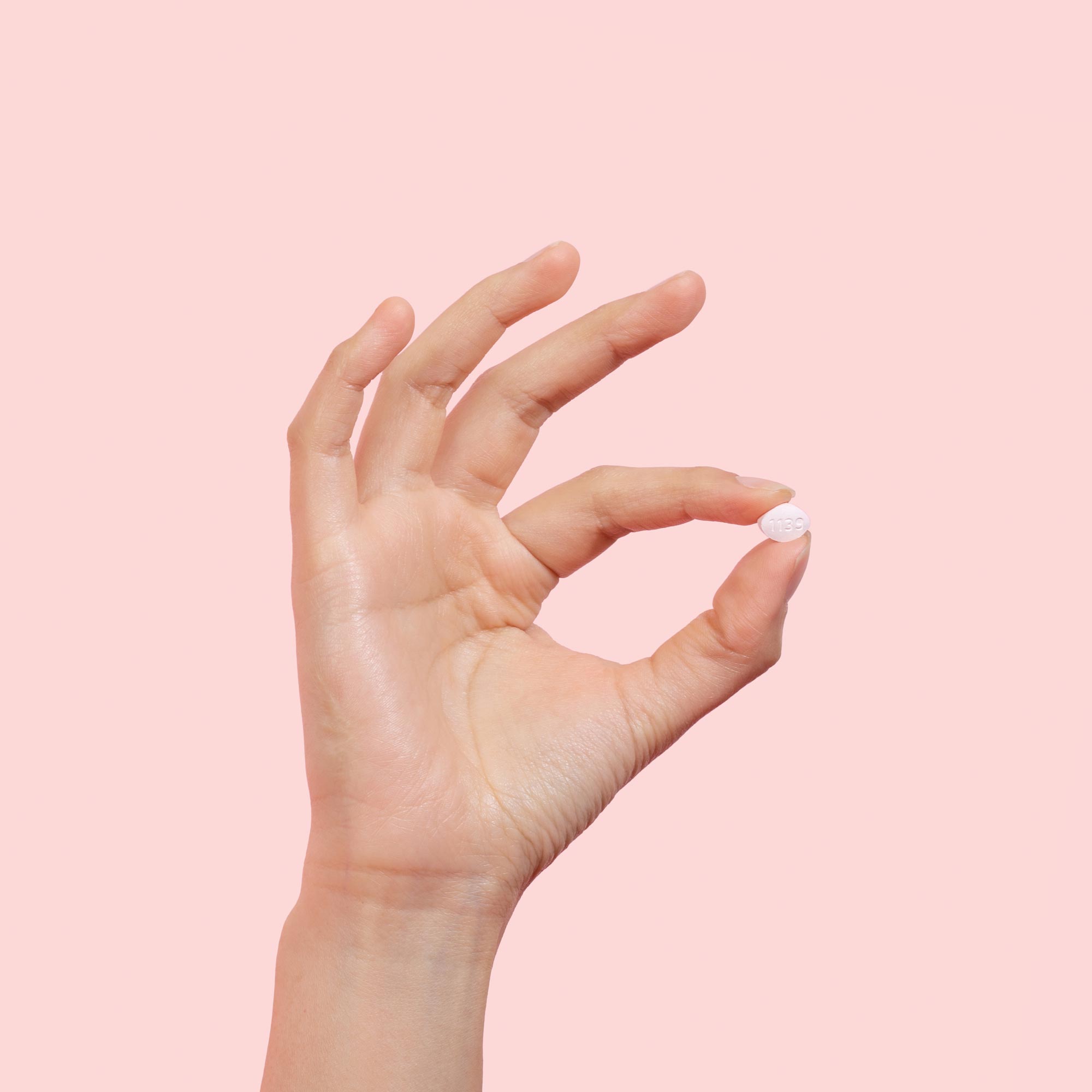 Woman's hand holding antifungal pill to treat yeast infections on a pink background