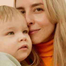 A blonde woman wearing an orange turtleneck holding her son