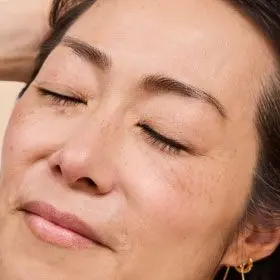 An asian woman with a pleasant look on her face has her hands through her hair