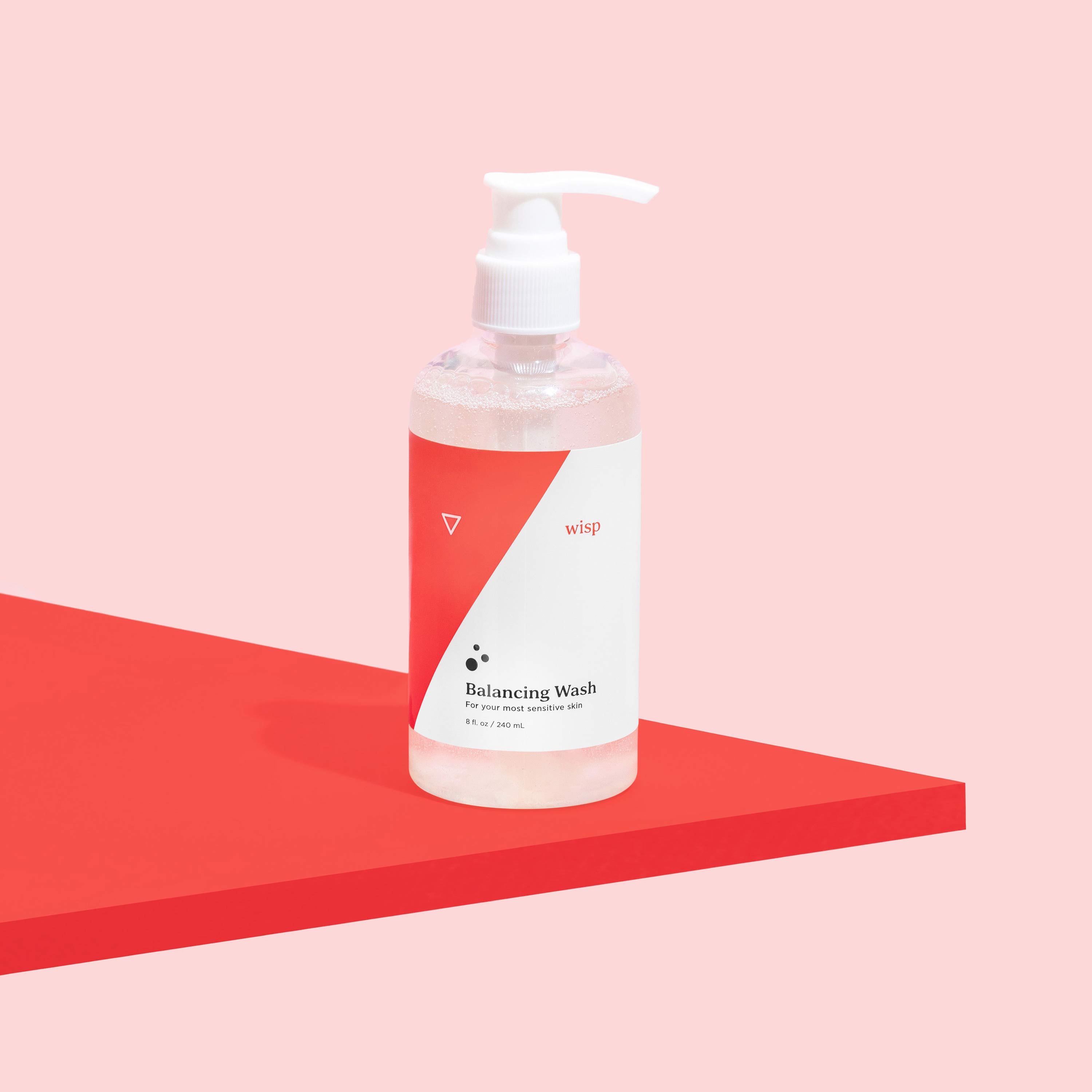 Bottle of Wisp Balancing Wash for intimate care on a pink background and red surface