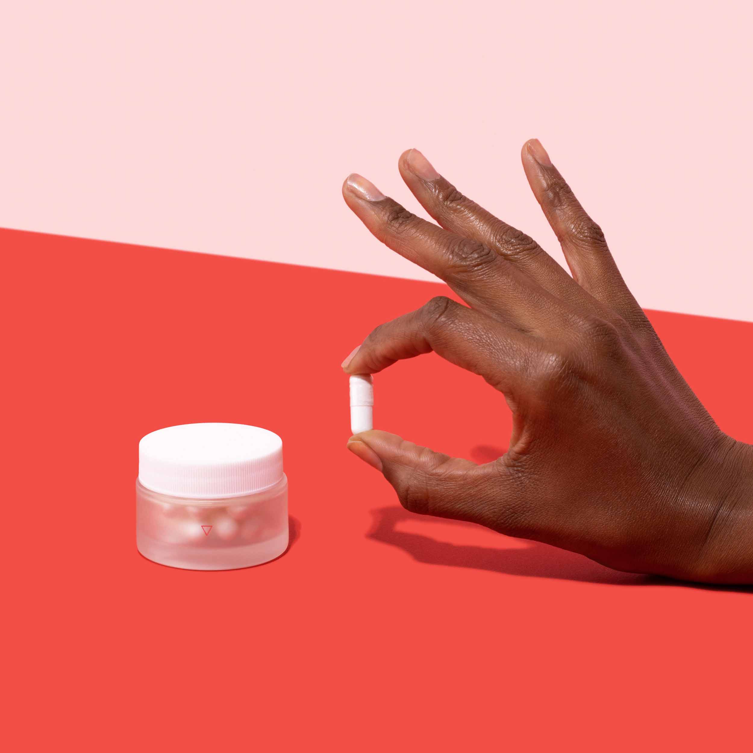 Jar of boric acid suppositories and hand holding suppository on red surface, on pink background