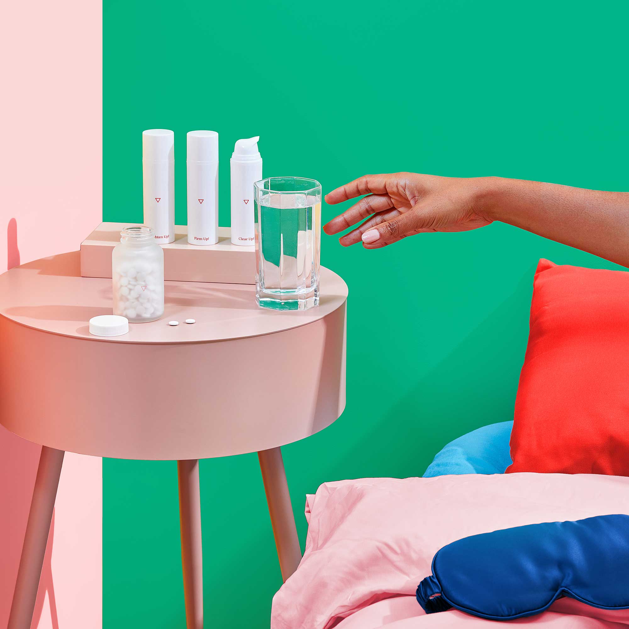 Woman's hand reaches for glass of water next to Wisp Skincare bottles on her bedside table