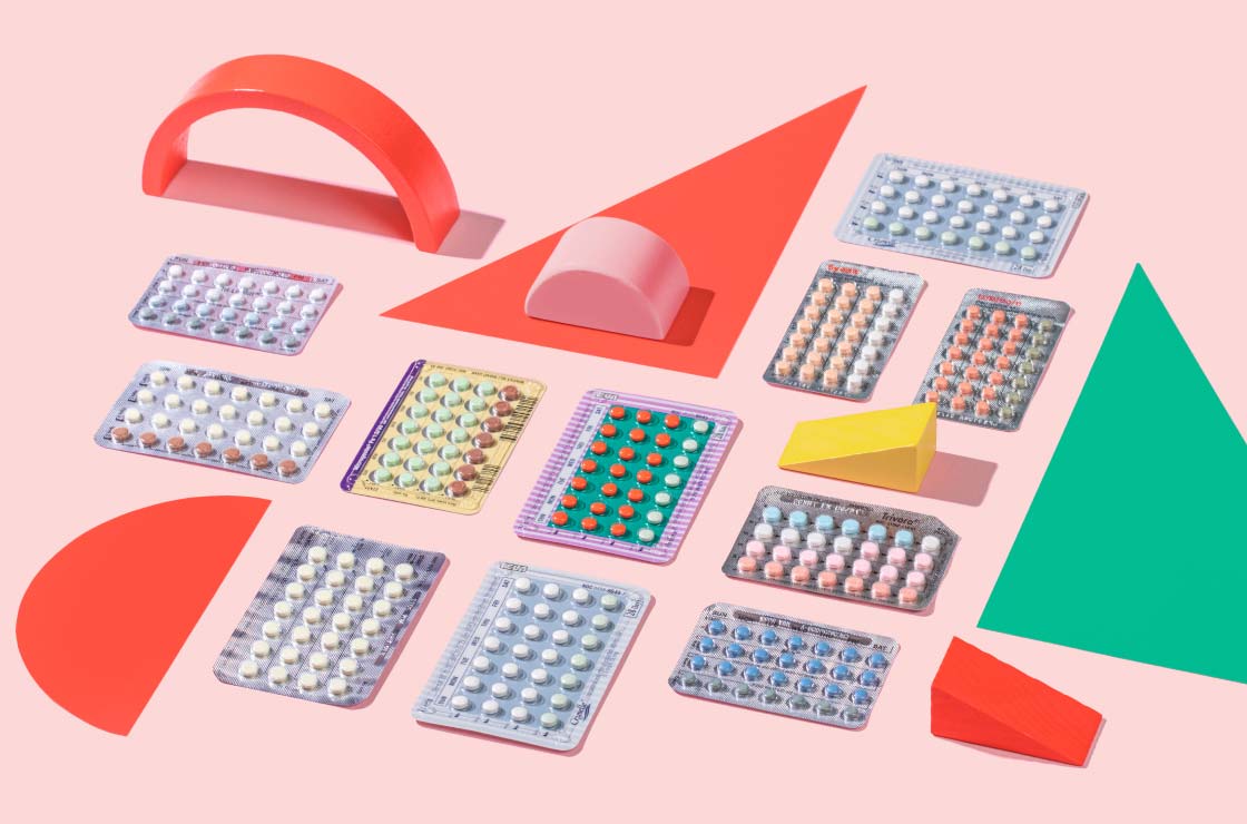 A flatlay of multiple birth control packets with colorful abstract shapes on a pink surface