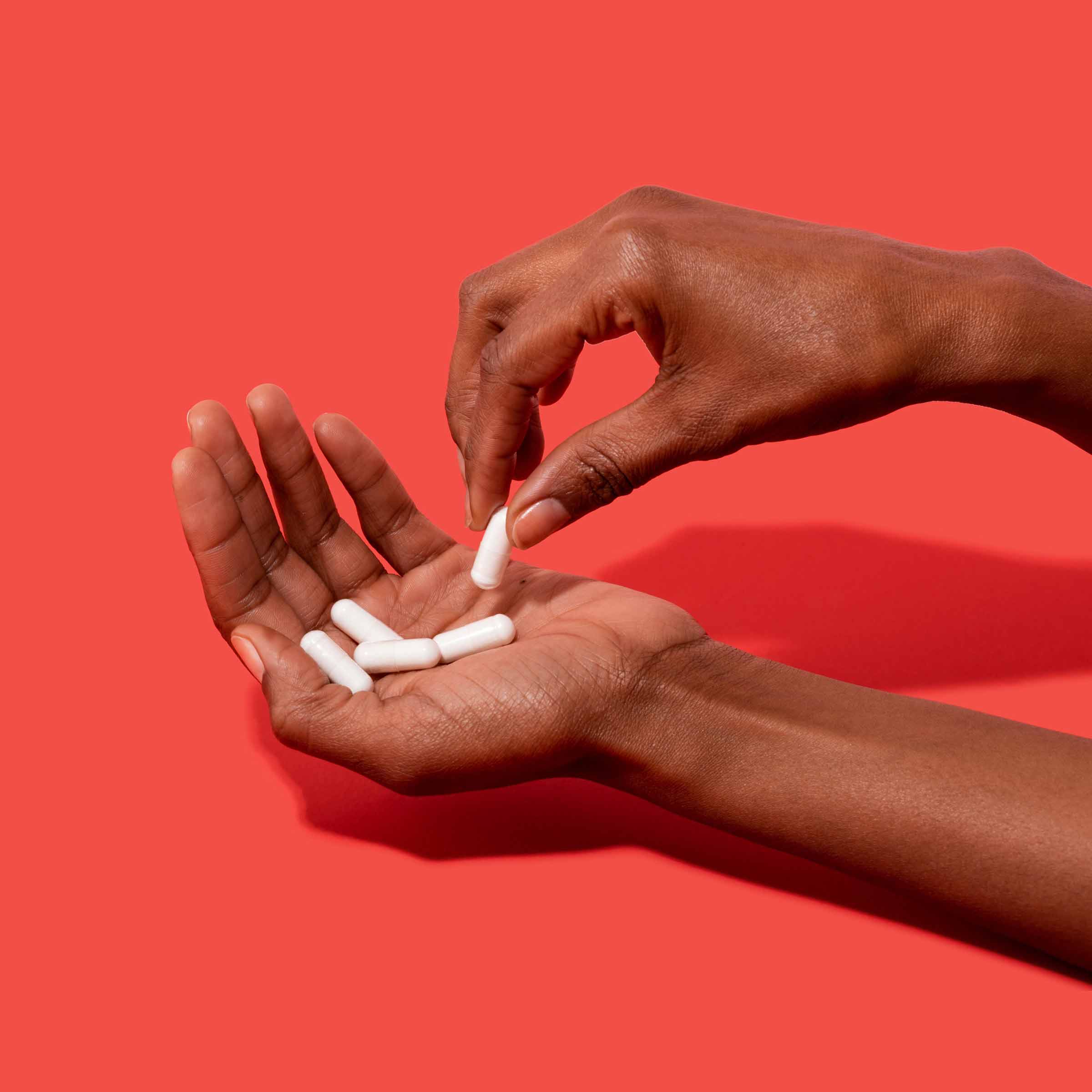 Hands holding D-Mannose capsules to prevent UTI on a red background