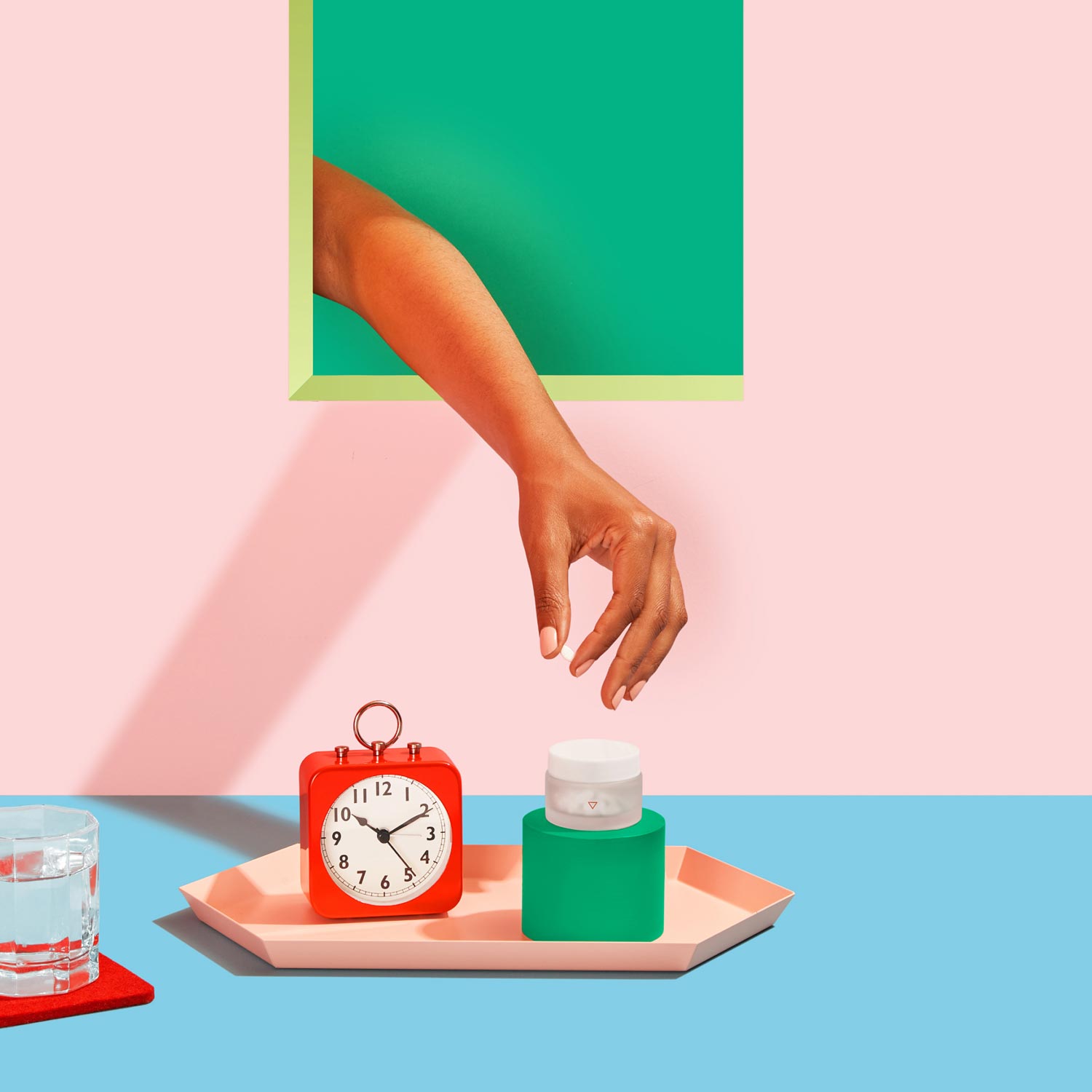 Woman's hand reaching for medication on pink and blue background with alarm clock