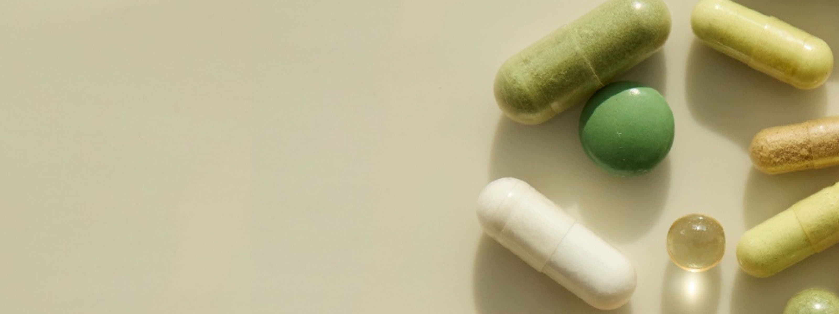 Assorted supplement capsules and softgels scattered on a beige background
