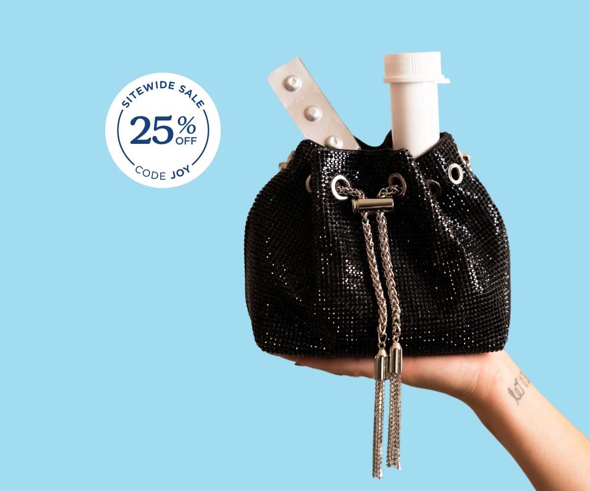 A woman's hand holding a black sparkly bag with a Wisp vial and a packet of zofran anti-nausea medication poking out of the top in front of a light blue background