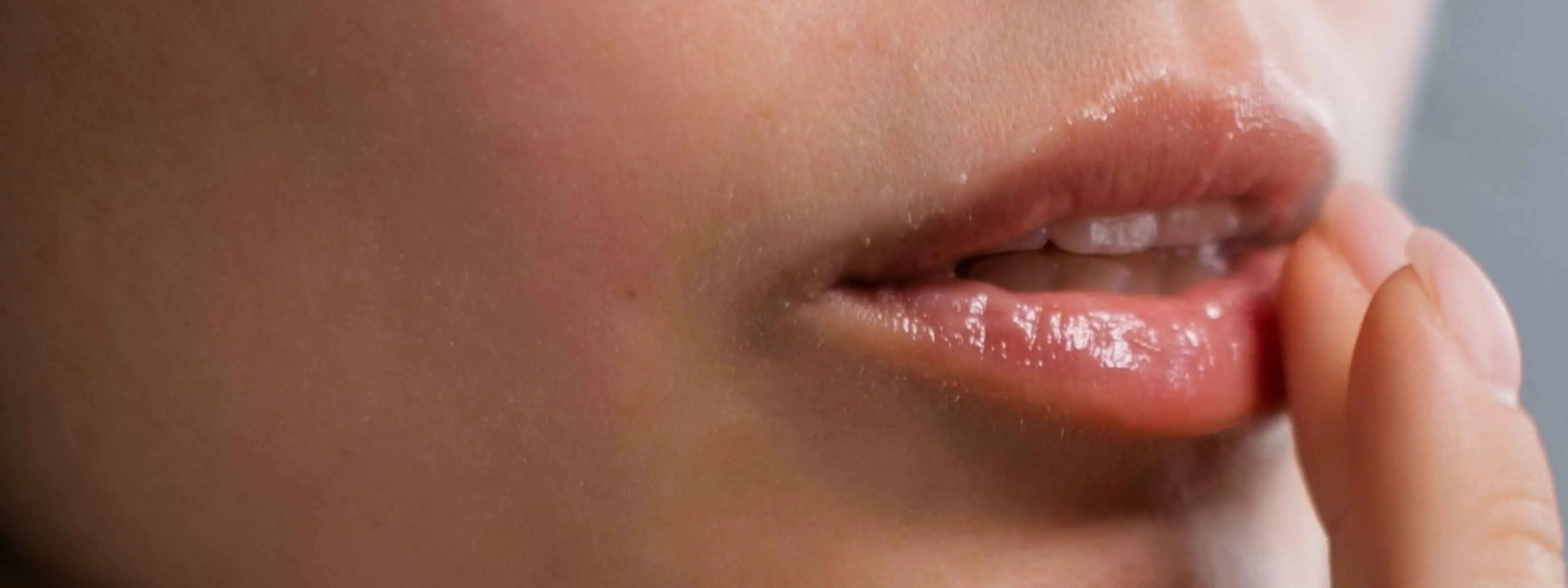 Close-up of a person's mouth and lower face, with a hand gently touching the corner of the lips.