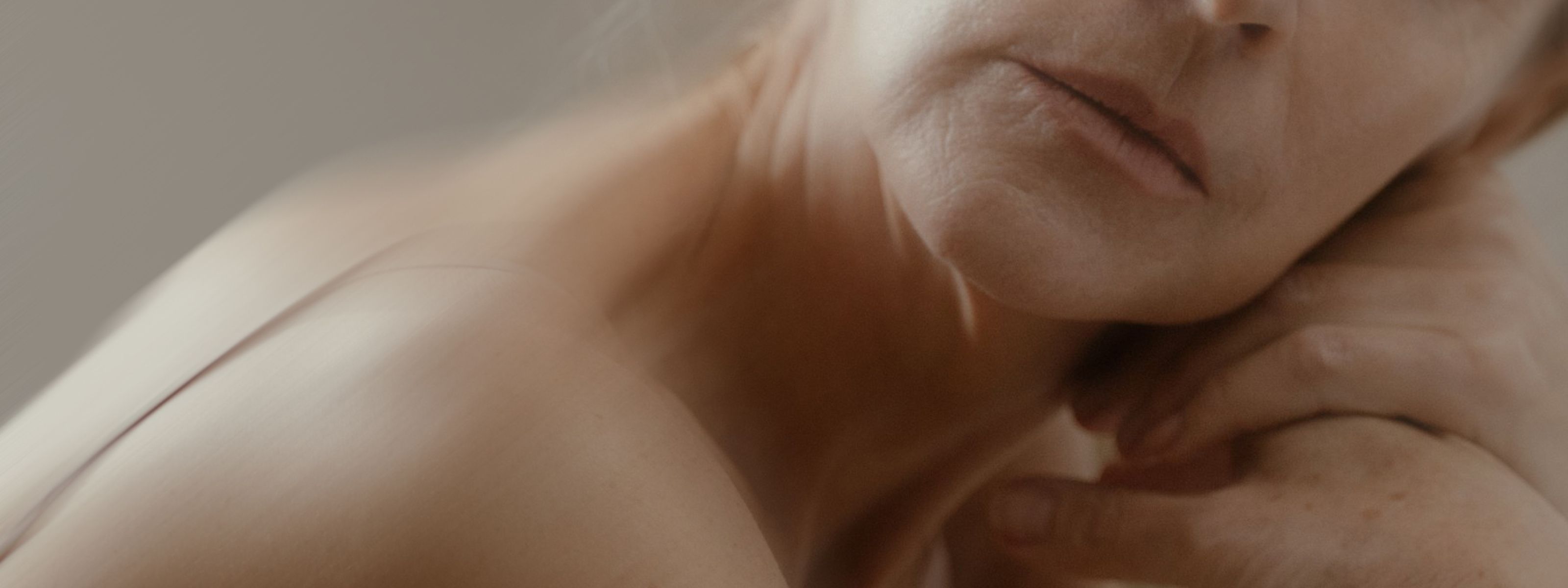 Close-up, artistic image of a person's lower face, neck, and bare shoulder, softly lit with warm tones, evoking themes related to hormone replacement therapy.
