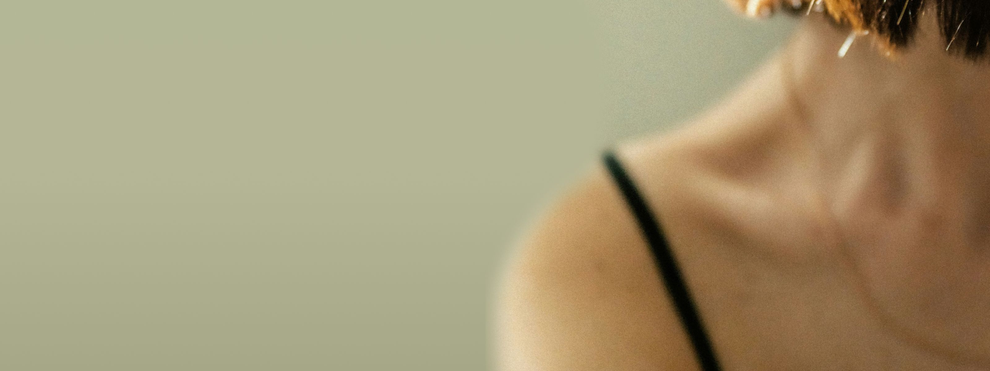 Close-up of a person’s shoulder and neck in a black spaghetti-strap top against blurred background