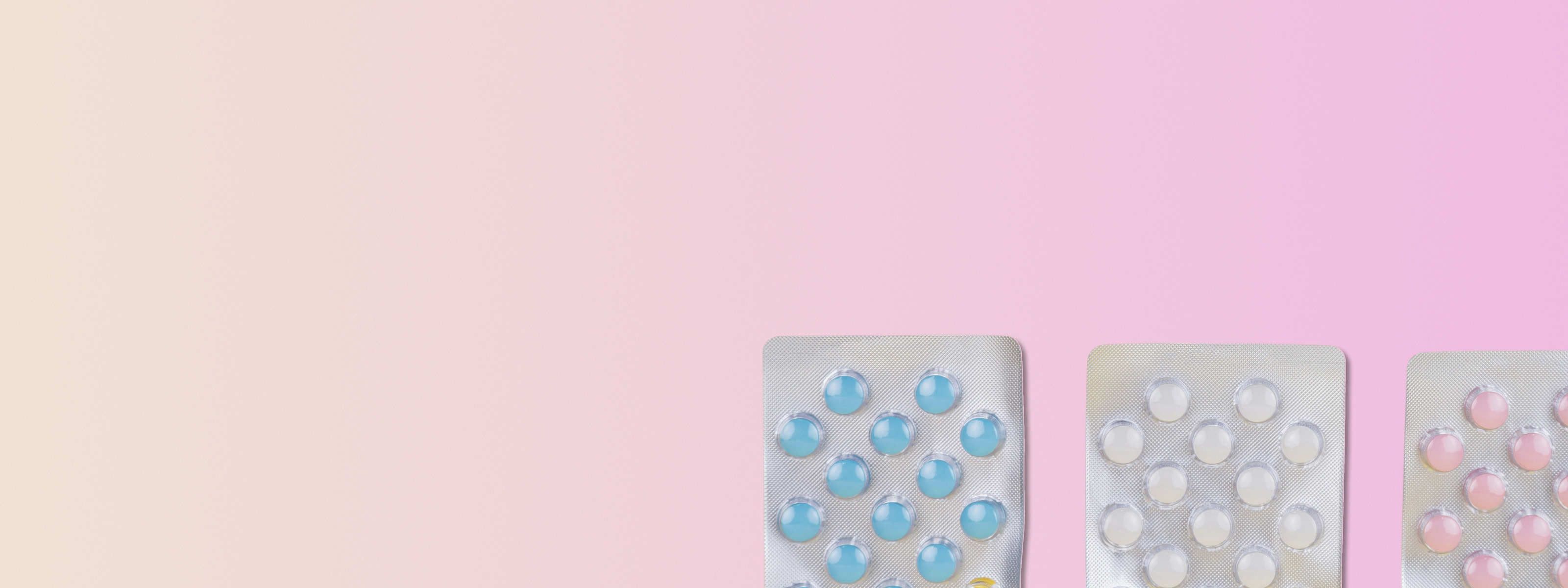 three birth control pill packs in front of a pink and beige background