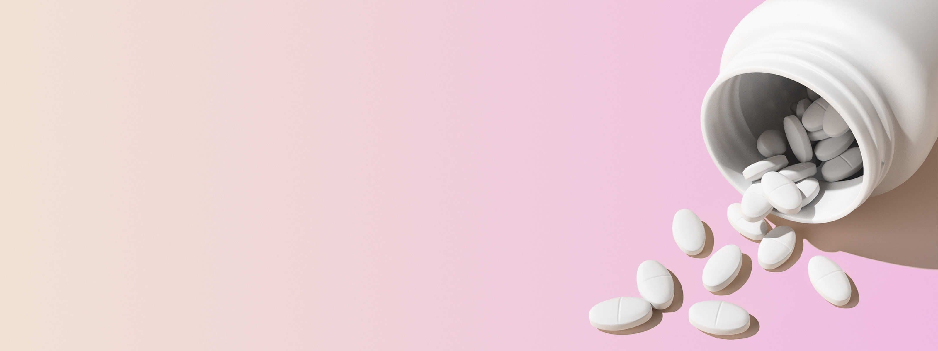 a tipped over white pill bottle with norethindrone tablets spilling out in front of a beige and pink background
