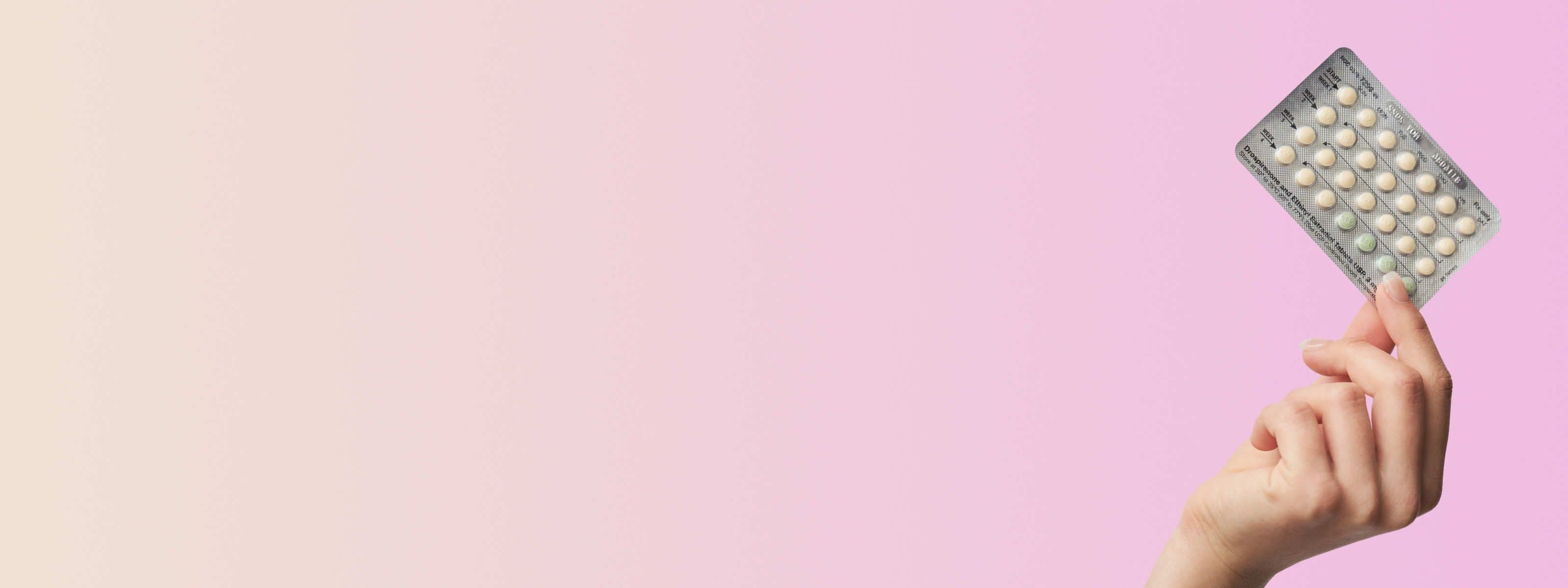 a hand holding a yaz birth control packet in front of a pink background