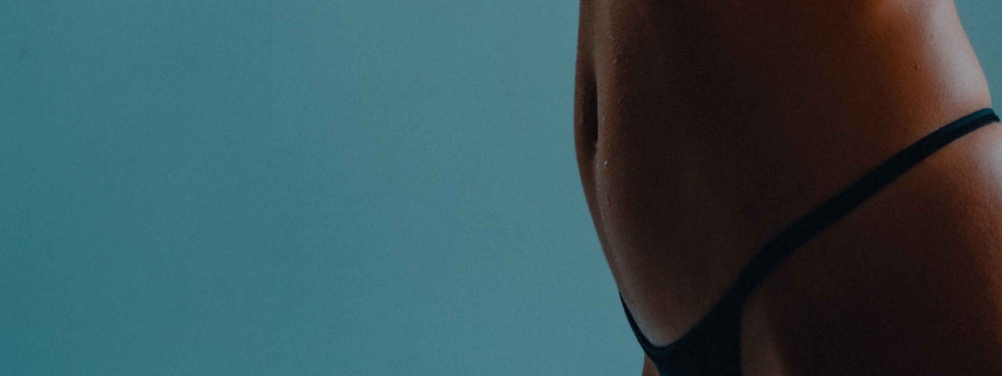 a side view image of a woman's stomach wearing black underwear in front of a turquoise background