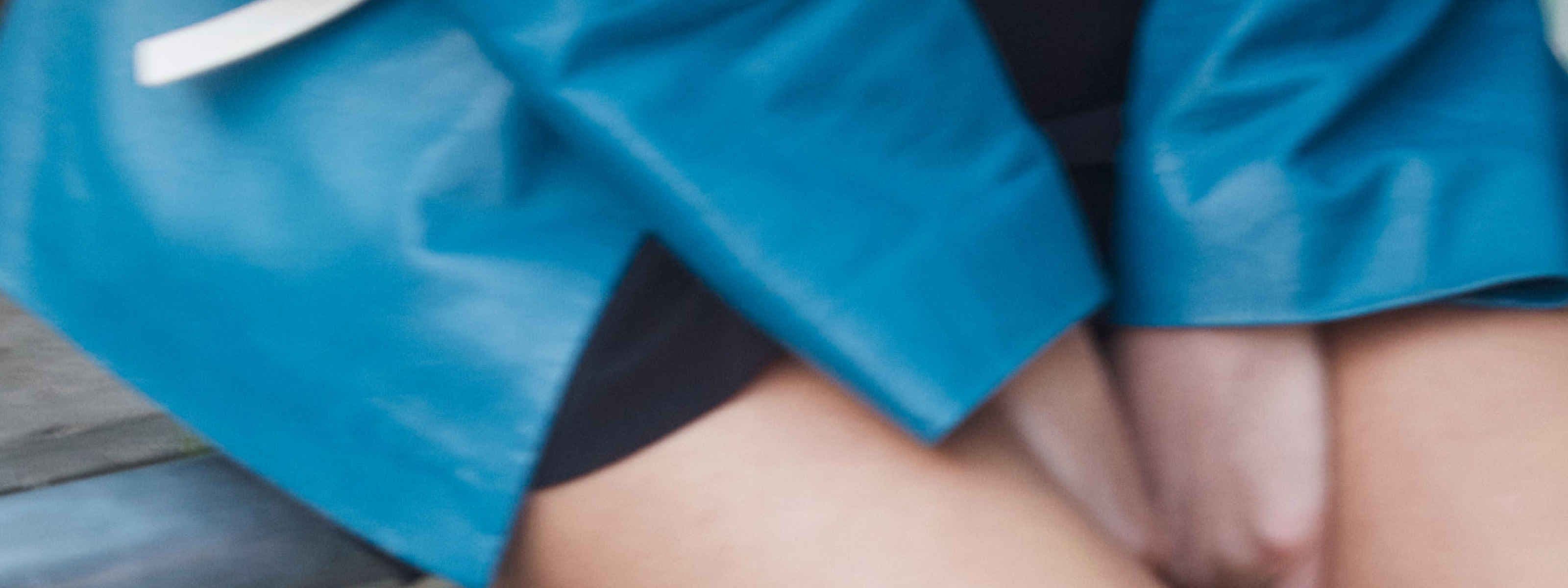 image of a person squeezing their hands in between their legs in a blue jacket