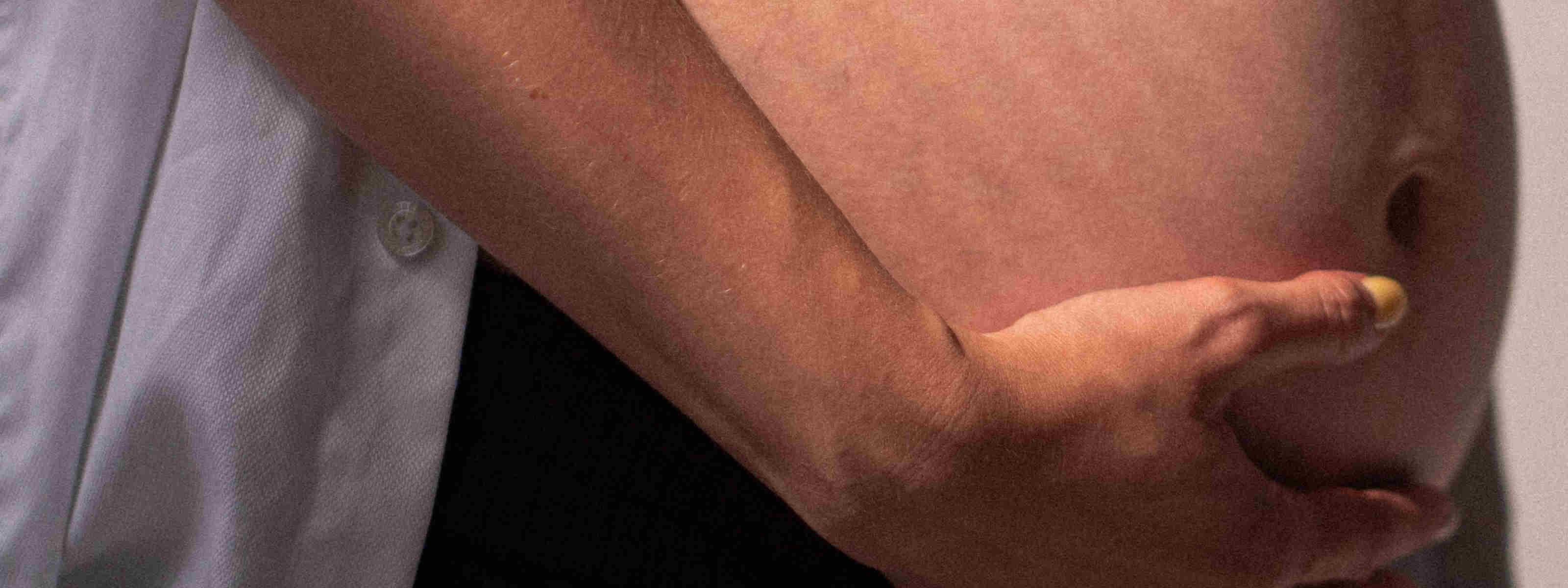 A pregnant person’s bare belly in profile, with their arm resting across it and hand cradling the underside.