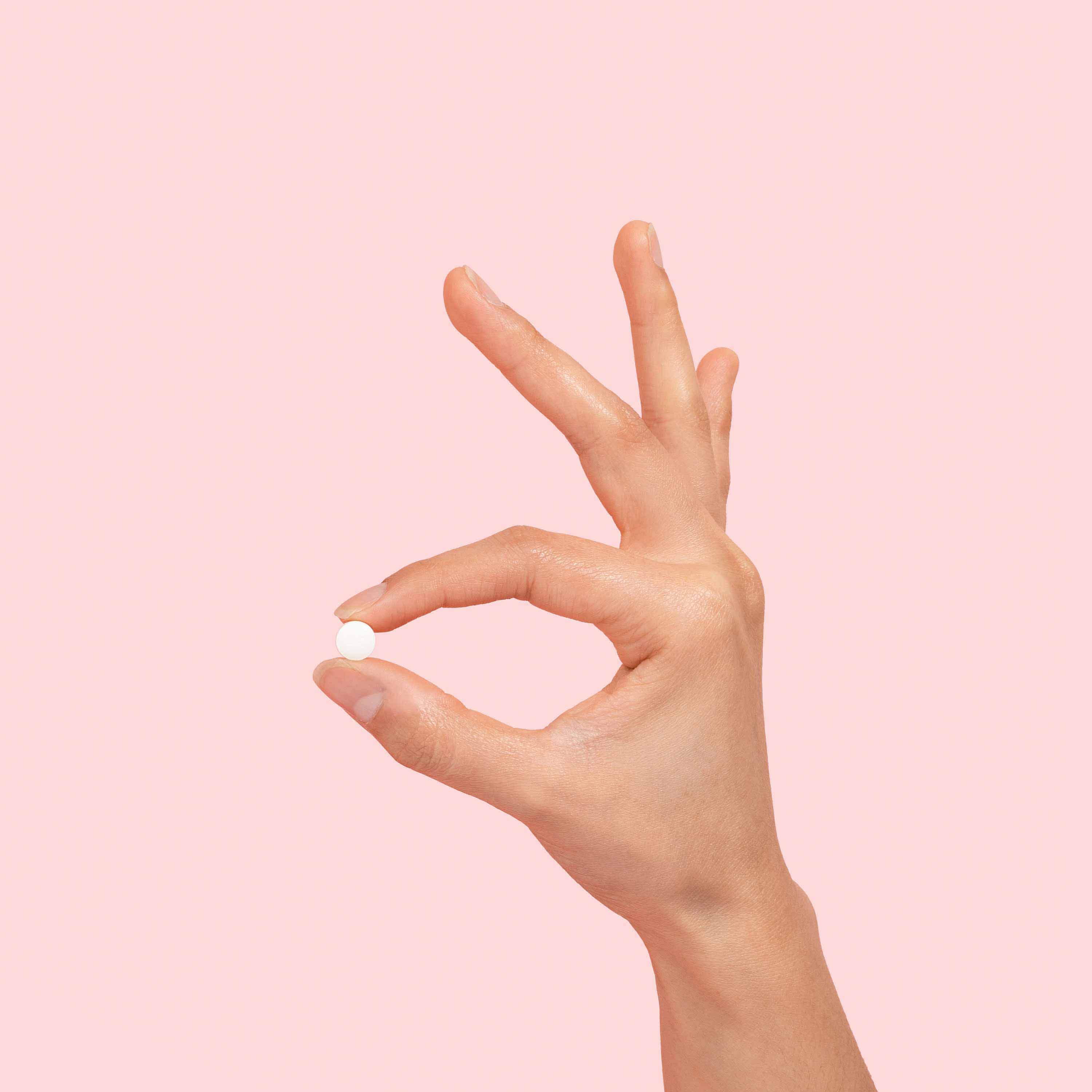 Hand holding Ella emergency contraception pill to prevent pregnancy on a pink background